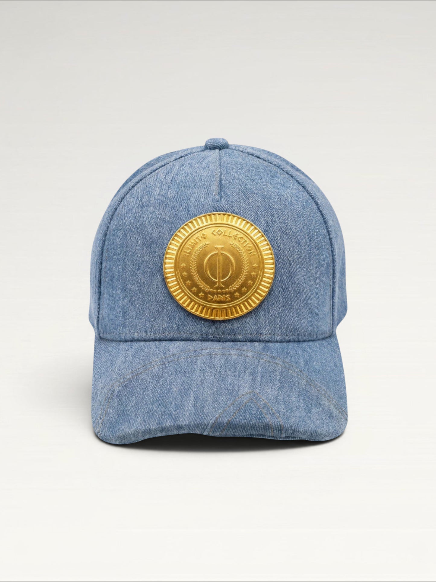 ILIMITO light blue denim baseball cap with curved brim and a central gold medallion emblem. Unisex fit.